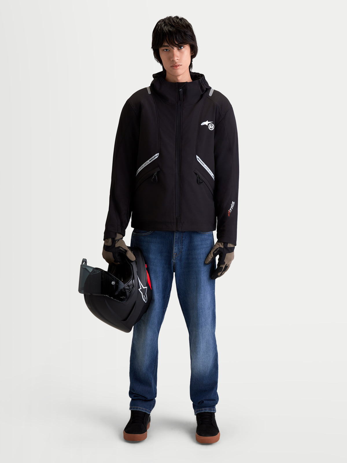 Alpinestars C-5 Drystar, chaqueta de moto urbana contemporánea para hombre, negra, vista frontal en modelo con vaqueros, guantes y sujetando un casco, con construcción softshell impermeable y capucha integrada
