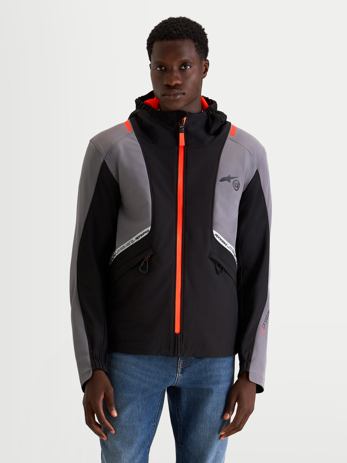 Alpinestars C 5 Drystar Chaqueta, chaqueta de moto urbana contemporánea para hombre en negro y gris oscuro, vista frontal en modelo que muestra construcción softshell impermeable, capucha integrada y detalles de cremallera en naranja brillante