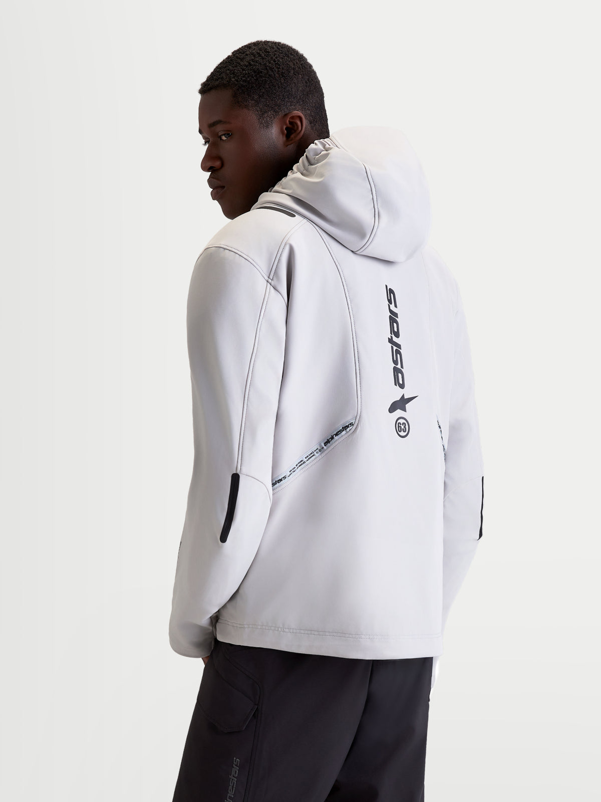 Chaqueta Alpinestars C 5 Drystar, chaqueta de moto urbana contemporánea para hombre en gris claro y negro, vista trasera en modelo con capucha integrada, construcción de softshell y detalles de logotipo vertical en la espalda