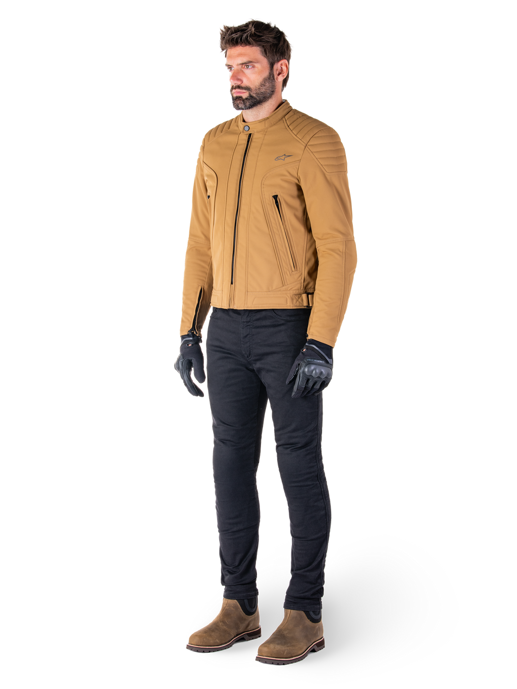Piloto masculino con la chaqueta Alpinestars Clayton WR en Utility Brown Light Gold, chaqueta de moto urbana contemporánea con detalles acolchados en los hombros, combinada con pantalones negros, guantes negros y botas marrones