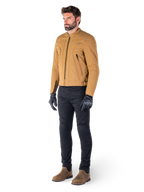 Piloto masculino con la chaqueta Alpinestars Clayton WR en Utility Brown Light Gold, chaqueta de moto urbana contemporánea con detalles acolchados en los hombros, combinada con pantalones negros, guantes negros y botas marrones