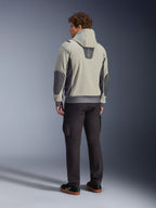 Modelo masculino visto desde atrás luciendo la chaqueta Alpinestars Moblast Waterproof en color Iron Gray Dark Sage, chaqueta urbana para moto con capucha con paneles laterales gris oscuro y parches reforzados en los codos, combinada con pantalones de conducción oscuros y zapatillas negras, estética minimalista moderna para desplazamientos urbanos.