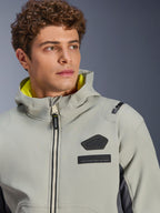 Chaqueta impermeable Alpinestars Moblast, Iron Gray Dark Sage, primer plano de un modelo masculino con la chaqueta, con el logotipo de Alpinestars en negro y parches MO.ST.EQ. en el pecho, forro de la capucha en amarillo brillante y un diseño técnico moderno.