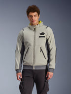 Alpinestars Moblast Waterproof Jacket, sudadera urbana para moto en gris claro y gris oscuro con forro de la capucha amarillo, bolsillos frontales y cremalleras negras, combinada con pantalones cargo negros, diseño deportivo moderno