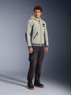 Chaqueta Alpinestars Moblast Waterproof, gris hierro y verde salvia oscuro, chaqueta de moto urbana con diseño de sudadera con capucha, usada por un modelo con pantalones de moto oscuros y botas negras, estética ciber-tecnológica minimalista con interior de capucha amarillo y cremalleras impermeables