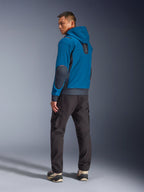 Chaqueta impermeable Alpinestars Moblast en colores Dark Petrol y Dark Navy, vista trasera en modelo mostrando el diseño con capucha, coderas e inserciones laterales en azul marino oscuro, combinada con pantalones cargo oscuros y zapatillas técnicas, ropa de moto urbana moderna.