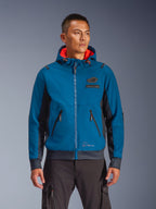 Alpinestars Moblast Waterproof Jacket usada por un modelo, chaqueta de moto para conducción urbana en azul y azul marino, diseño con capucha y forro interior rojo, cremalleras negras y detalle de parche en el pecho, equipamiento de moto inspirado en el streetwear