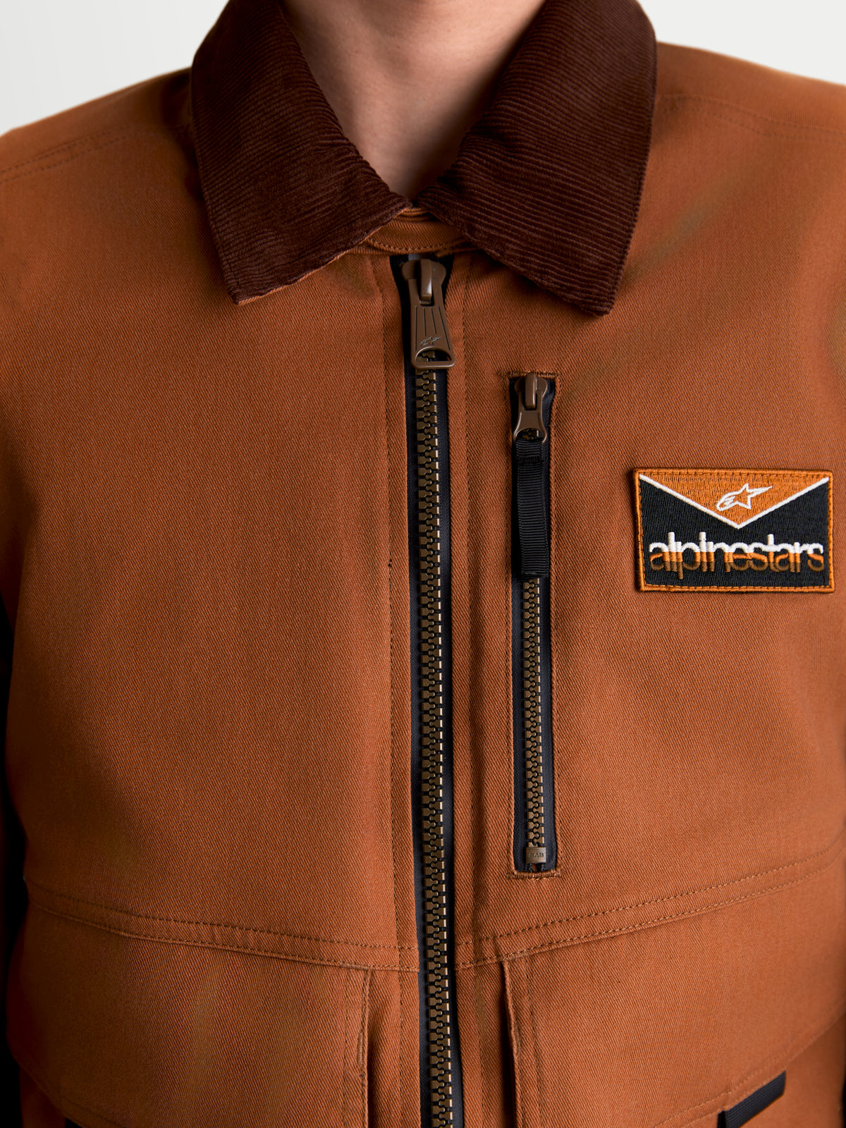 Alpinestars Mustang Waterproof Jacket, men's urban motorcycle textile jacket, dark rust and dark brown, close-up view of workwear-styled stretch twill construction, corduroy collar, front zipper, and chest logo patch