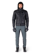 Chaqueta Alpinestars Mohobbs Waterproof en color negro, modelo masculino con chaqueta bomber acolchada y capucha, combinada con pantalones de conducción grises, guantes negros y botas negras, equipamiento de motociclismo urbano contemporáneo.