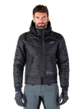 Alpinestars Mohobbs Waterproof Jacket, chaqueta bomber de moto negra acolchada, tejido de poliéster acolchado con cremallera frontal y bolsillos con cremallera, pequeño logo blanco en el pecho, usada por un modelo con pantalones grises y guantes, diseño de estilo urbano para conducción en ciudad