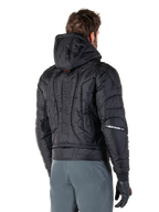Chaqueta Alpinestars Mohobbs Waterproof, negra, vista trasera que muestra la construcción acolchada, capucha, marca denominativa 'astars' vertical en la espalda y logotipos de Alpinestars en las mangas, usada con pantalones grises y guantes negros.