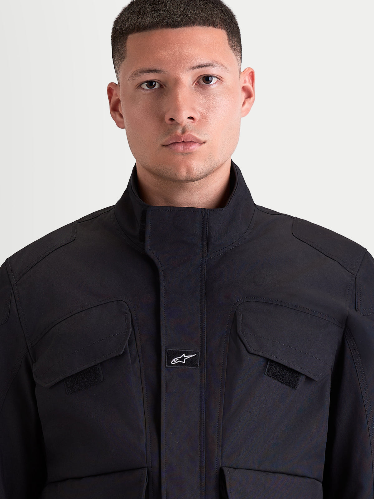 Alpinestars Altan Drystar Chaqueta, chaqueta de moto urbana contemporánea para hombre en color negro, vista frontal en primer plano que muestra la construcción de tejido técnico mate, el cuello cálido integrado y los bolsillos cargo en el pecho en un modelo