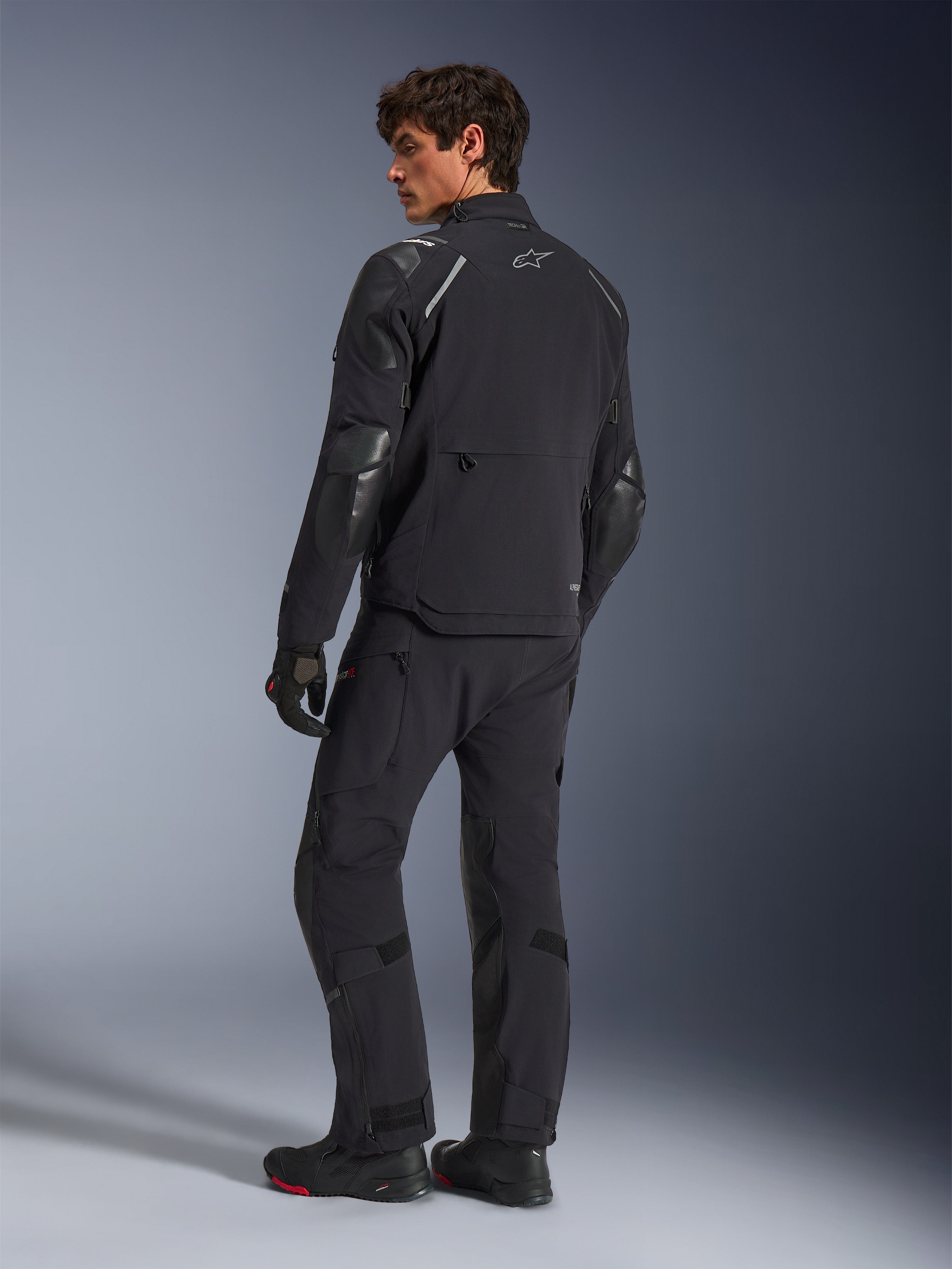 Chaqueta Alpinestars Andes Pro Drystar® XF, chaqueta de motociclismo de aventura, negra, vista trasera con pantalones y botas a juego, con paneles reforzados y el logotipo de la estrella plateada, equipamiento técnico de conducción para todo tipo de clima