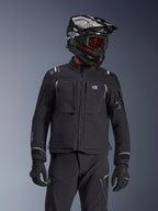 Motociclista de aventura con la chaqueta Alpinestars Andes Pro Drystar® XF en color negro y gris oscuro, con el logotipo All Terra en el pecho, combinada con pantalones técnicos a juego y un casco de aventura negro con gafas, conjunto de equipamiento profesional para touring.