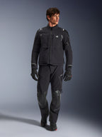 Modelo masculino con chaqueta Alpinestars Andes Pro Drystar® XF, chaqueta de moto de aventura en negro y gris oscuro, combinada con pantalones técnicos y guantes a juego, con múltiples bolsillos y logotipo 'Terra' en el pecho.