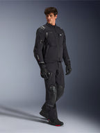 Chaqueta Alpinestars Andes Pro Drystar® XF, chaqueta de moto negra y gris oscuro, vestida por un modelo masculino con pantalones de aventura, guantes y botas a juego, toma de estudio de cuerpo completo, equipamiento técnico para touring de aventura con detalles reflectantes y logotipos
