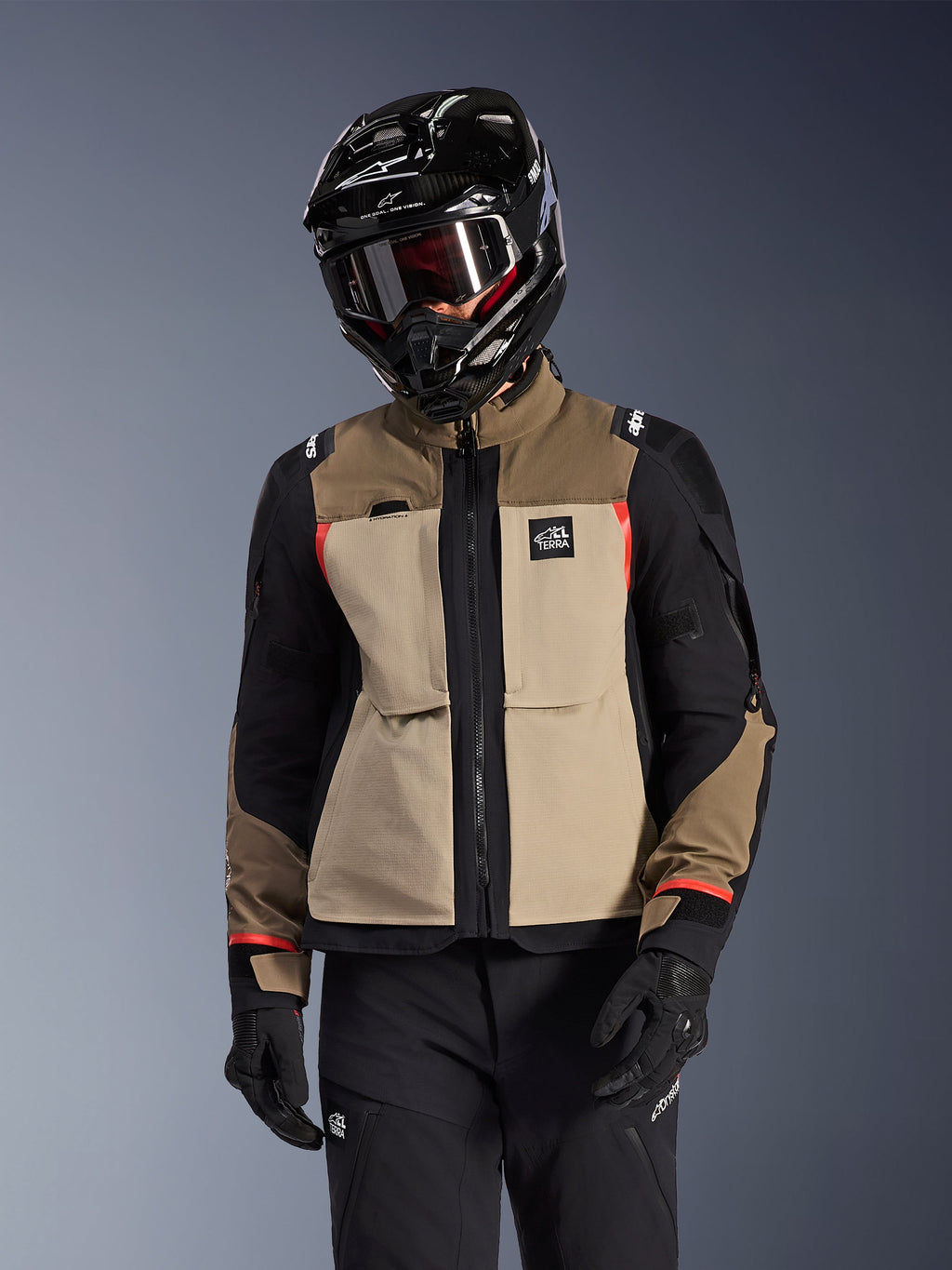 Chaqueta Alpinestars Andes Pro Drystar® XF, chaqueta de motociclismo Adventure Touring, color Walnut Aluminum beige y marrón con paneles negros y detalles rojos, usada con casco y gafas Alpinestars negros, equipamiento técnico de motociclismo para exteriores