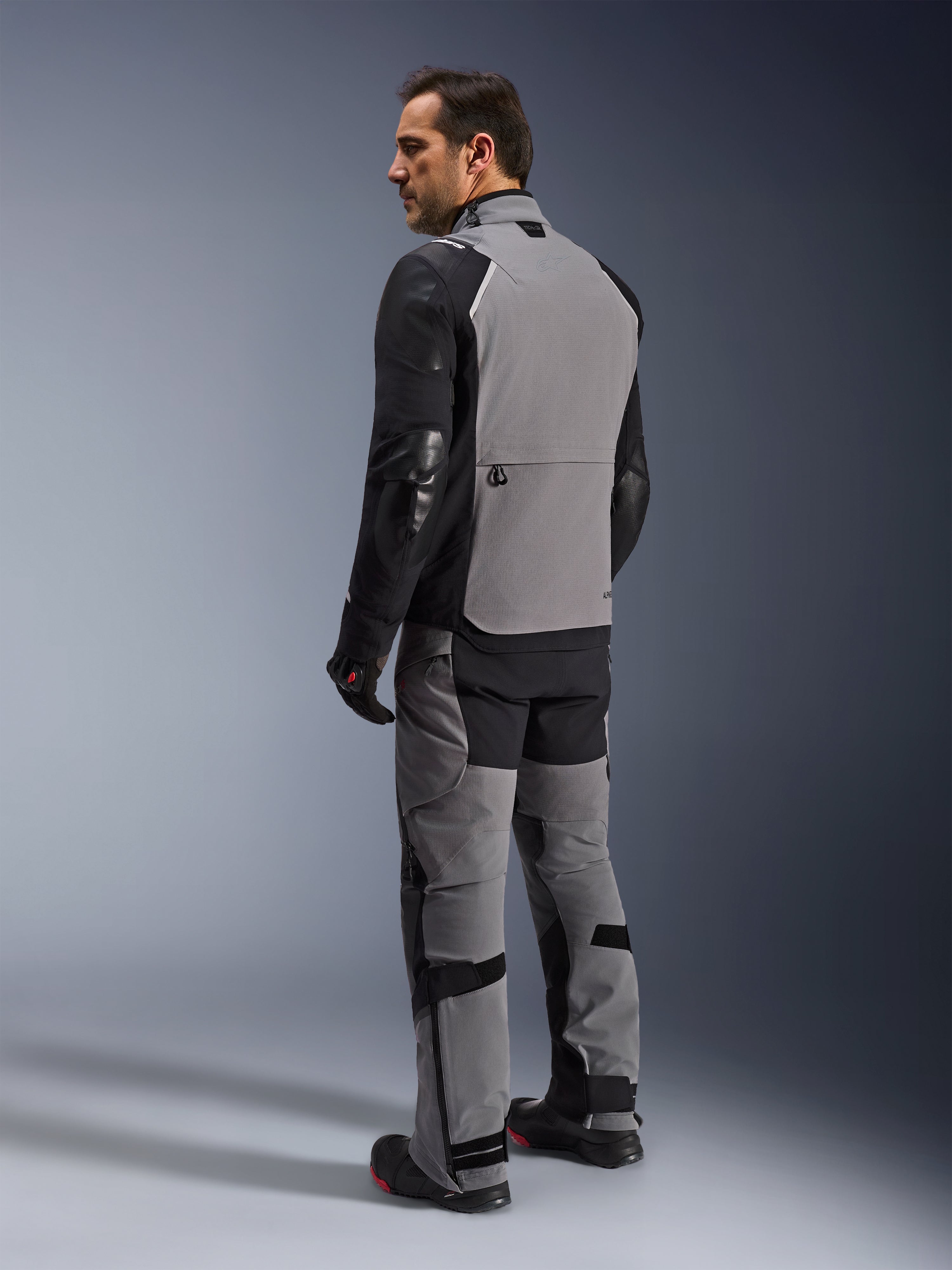 Chaqueta Alpinestars Andes Pro Drystar® XF, chaqueta de motociclismo adventure-touring en gris oscuro y negro, vista trasera en un modelo que muestra el panel posterior grande y las mangas reforzadas, combinada con pantalones de aventura, guantes y botas a juego