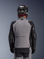 Chaqueta Alpinestars Andes Pro Drystar® XF, gris oscuro y negro, vista trasera que muestra el gran bolsillo de almacenamiento posterior y la marca Tech-Air, usada por un motorista con casco negro y pantalones de conducción a juego, equipamiento profesional para touring de aventura