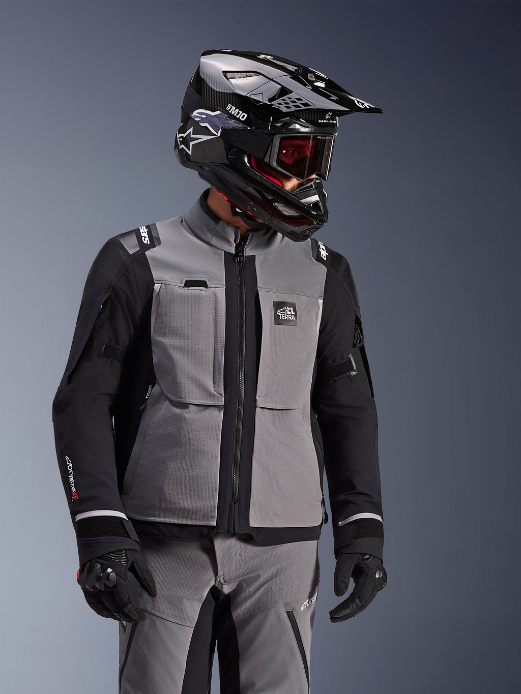 Chaqueta Alpinestars Andes Pro Drystar® XF, gris oscuro y negro, chaqueta de moto de aventura usada con casco SM10 negro y equipamiento de conducción a juego, diseño textil de 3 capas con cremallera central y bolsillos en el pecho, diseño articulado para touring en todo tipo de clima