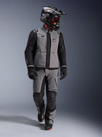 Motociclista de aventura con chaqueta Alpinestars Andes Pro Drystar® XF en gris oscuro y negro, pantalones de aventura a juego, casco Alpinestars negro con gafas, guantes y botas negros, equipamiento técnico completo de touring para viajes de larga distancia
