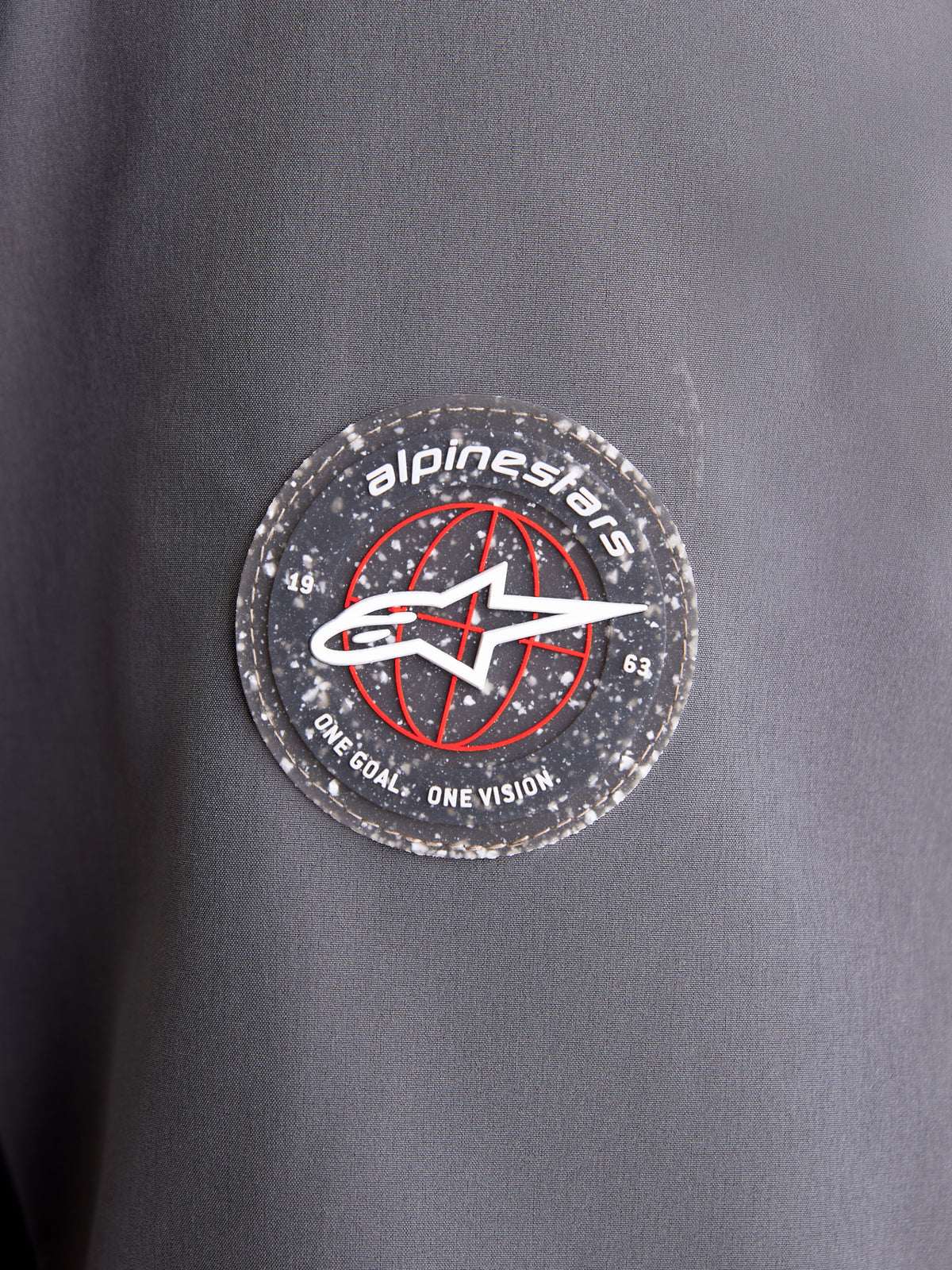 Alpinestars Therma Tech Wp Jk, chaqueta de moto impermeable, detalle en primer plano del parche circular con el logotipo de la marca en la manga de tejido gris oscuro y negro