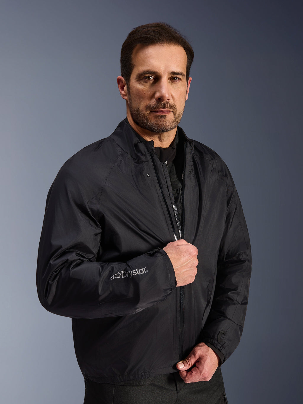 Chaqueta Alpinestars Cusco Drystar®, capa de membrana impermeable negra usada por un modelo masculino, con el logotipo Drystar en la manga, equipamiento ligero de motociclismo para adventure touring