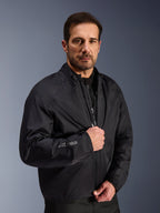 Chaqueta Alpinestars Cusco Drystar®, capa de membrana impermeable negra usada por un modelo masculino, con el logotipo Drystar en la manga, equipamiento ligero de motociclismo para adventure touring