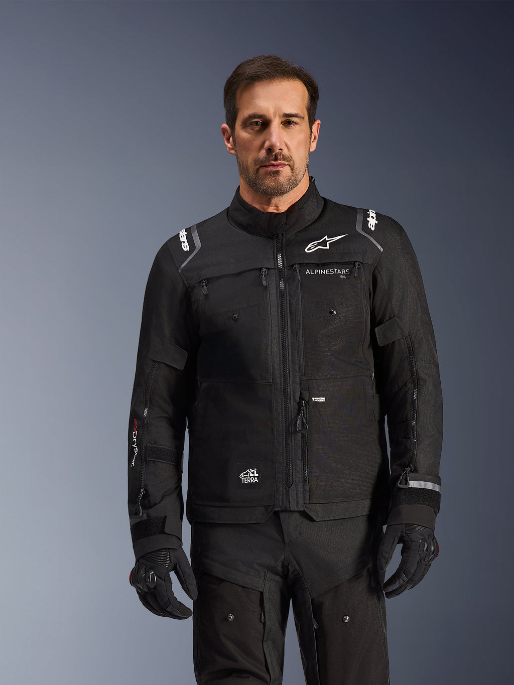 Chaqueta Cusco Drystar® de Alpinestars, chaqueta de motociclismo negra, vestida por un modelo con guantes y pantalones negros a juego, con construcción de tejido técnico y logotipos blancos de Alpinestars, diseñada para el adventure touring por carretera