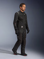 Modelo masculino vistiendo la chaqueta Alpinestars Cusco Drystar® en color negro, equipamiento de motociclismo adventure touring con pantalones y botas negras a juego, con un diseño multibolsillo, marca 'Drystar' en la manga y parche con el logo 'Terra'.