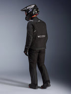 Chaqueta Alpinestars Cusco Drystar® en color negro, vista lateral trasera de un motorista con un conjunto completo de adventure touring que incluye pantalones y guantes negros a juego, casco de aventura negro, confección textil con logotipos reflectantes en la espalda