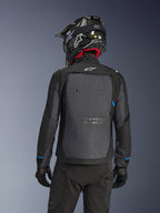 Motociclista visto desde atrás con la chaqueta Alpinestars Cusco Drystar® en color negro y gris oscuro, con un gran panel de ventilación trasero gris y logo blanco, combinado con un casco off-road negro y equipamiento de conducción para adventure touring.