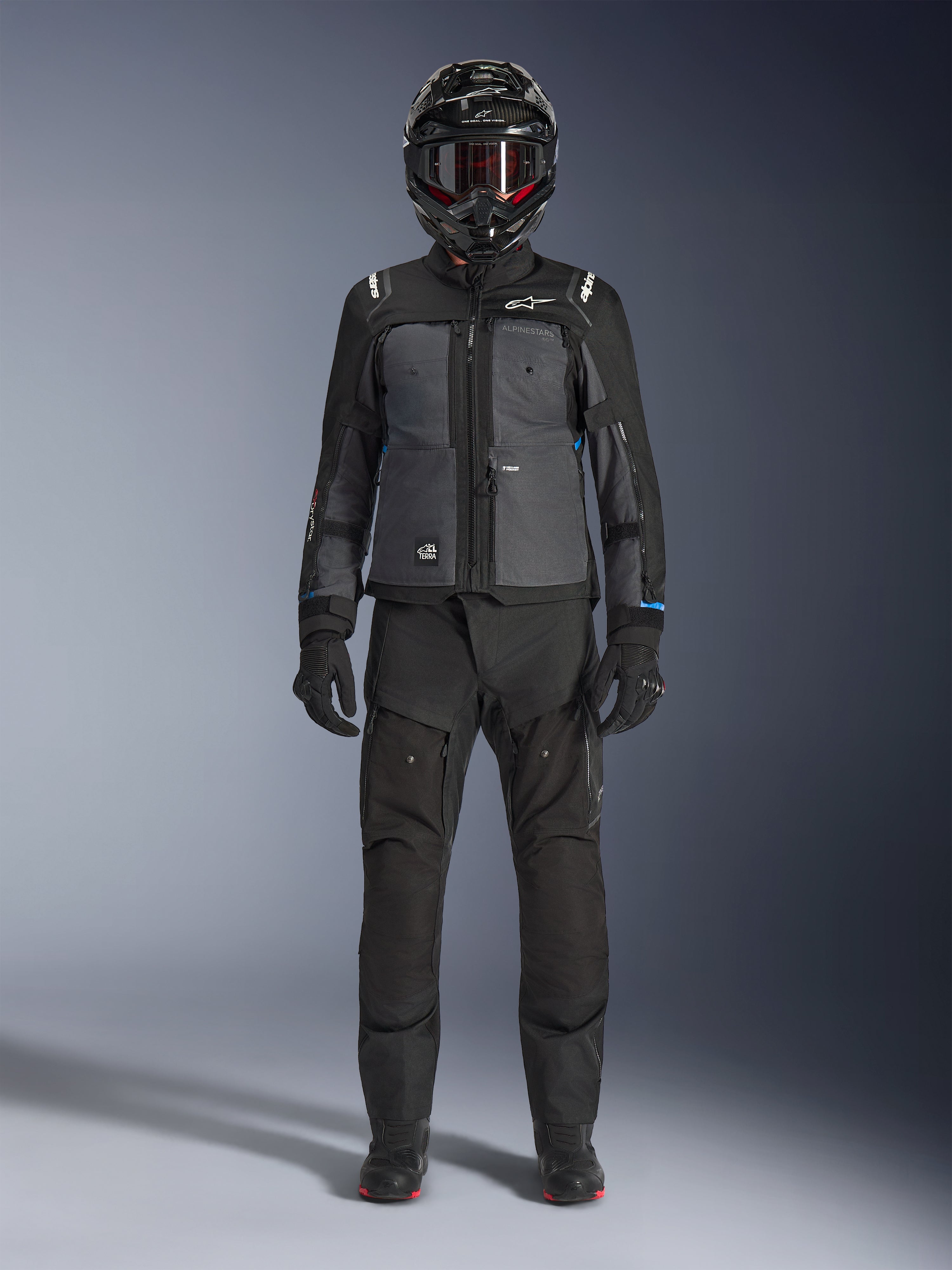 Chaqueta Alpinestars Cusco Drystar®, chaqueta adventure touring en color negro y gris oscuro, combinada con pantalones negros a juego, guantes y casco integral, vista frontal de cuerpo completo, ropa de protección para motociclista