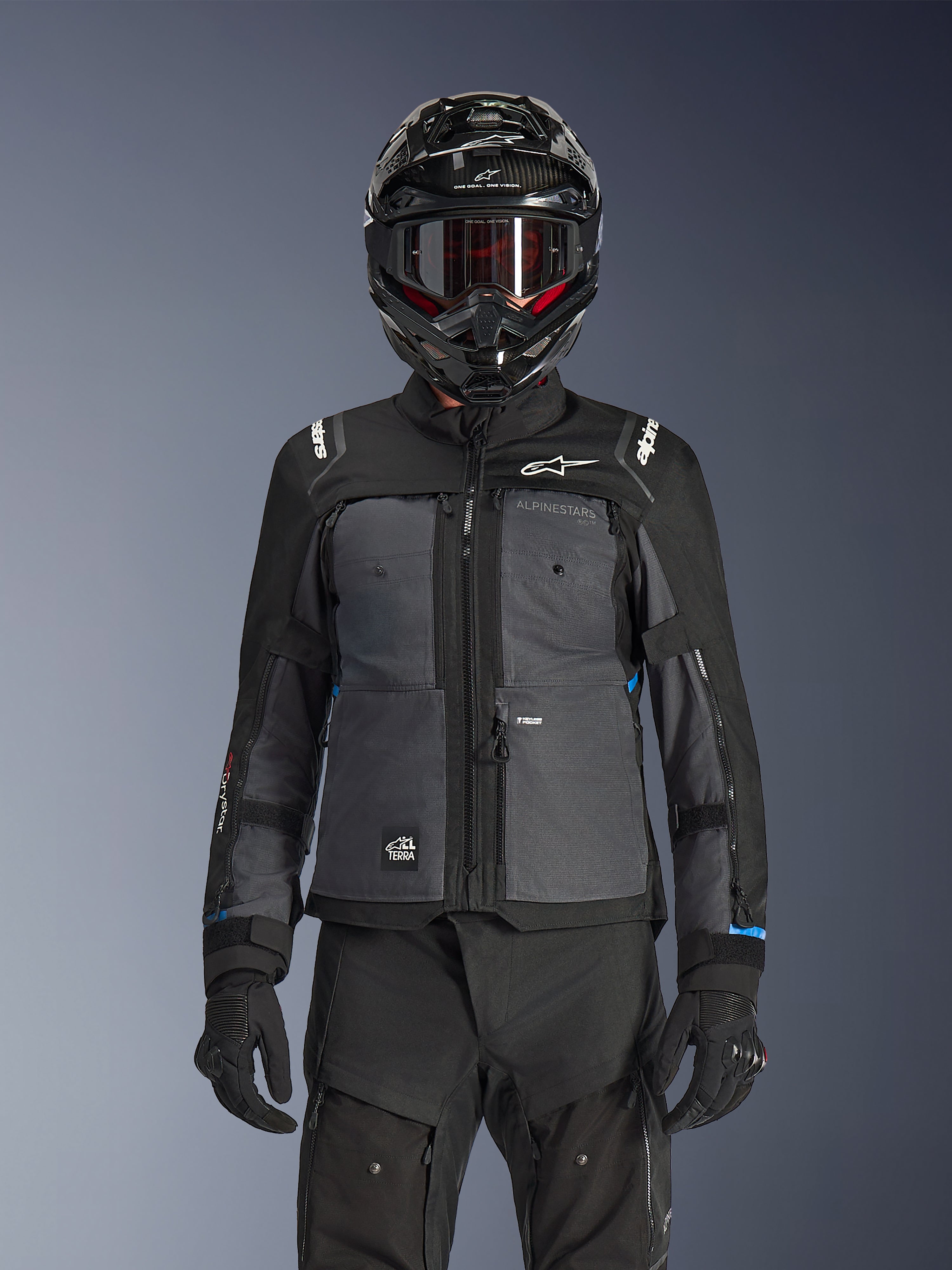 Chaqueta Alpinestars Cusco Drystar®, negro y gris oscuro, chaqueta de adventure touring para motocicleta usada con pantalones técnicos negros a juego y un casco dual-sport, con un diseño en dos tonos con paneles de ripstop y logotipos de Alpinestars