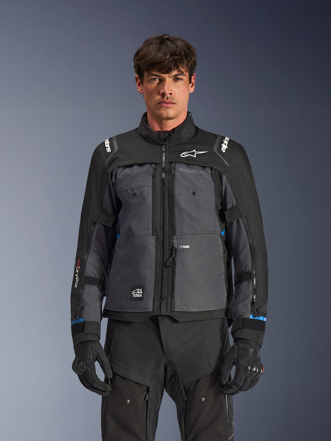 Chaqueta Alpinestars Cusco Drystar®, chaqueta de mototurismo, negro y gris oscuro, vista frontal en modelo, con logotipos de Alpinestars en el pecho y los hombros, marca Drystar® en la manga, diseño técnico multibolsillo con cremalleras de ventilación, combinada con equipamiento de conducción negro