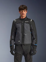 Chaqueta Alpinestars Cusco Drystar®, chaqueta de mototurismo, negro y gris oscuro, vista frontal en modelo, con logotipos de Alpinestars en el pecho y los hombros, marca Drystar® en la manga, diseño técnico multibolsillo con cremalleras de ventilación, combinada con equipamiento de conducción negro