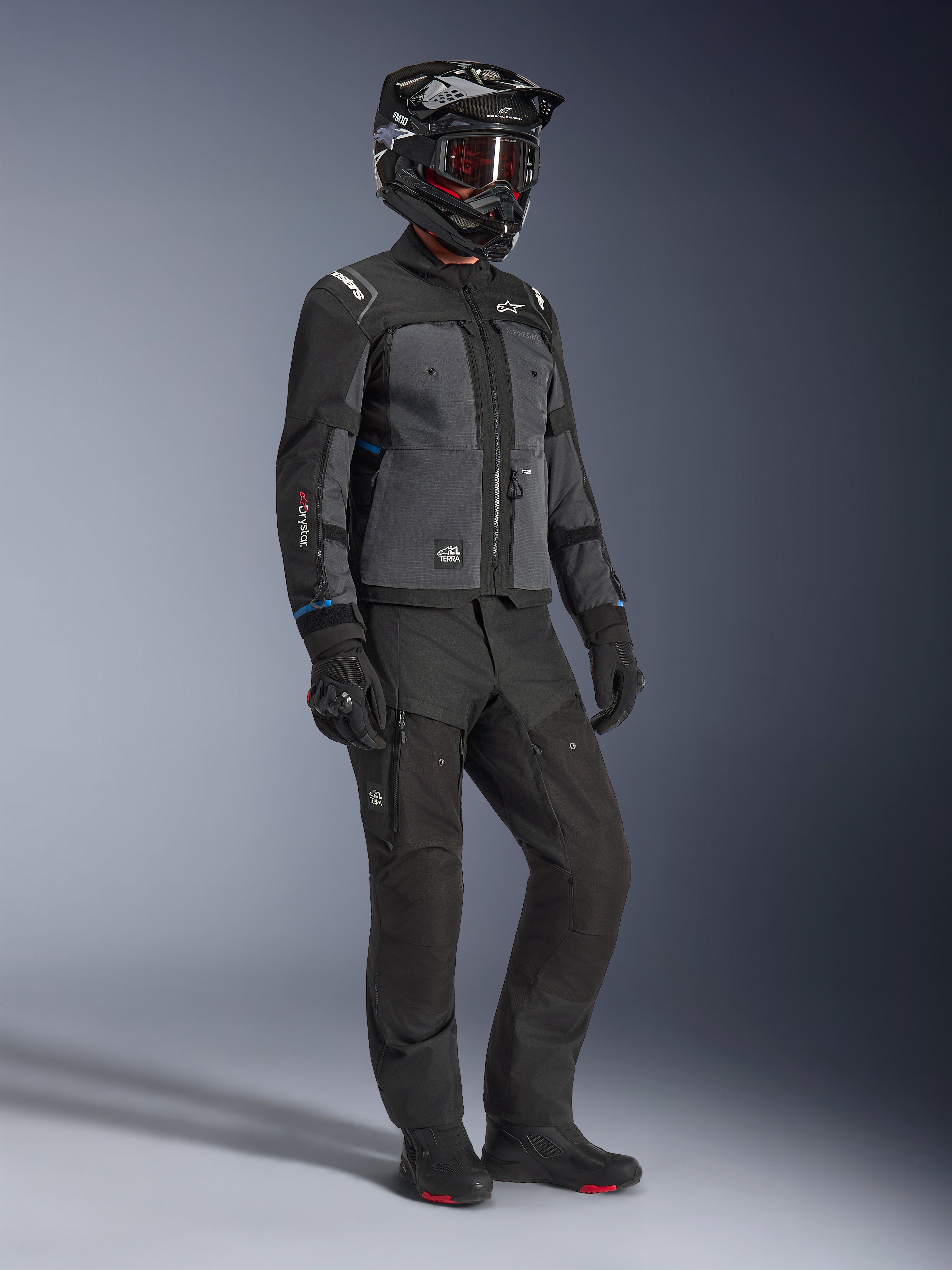 Modelo con la chaqueta Alpinestars Cusco Drystar® en Negro y Gris Profundo, equipamiento completo de motociclismo con casco negro, pantalones técnicos a juego, guantes y botas; construcción en ripstop y softshell para conducción por carretera y adventure touring.