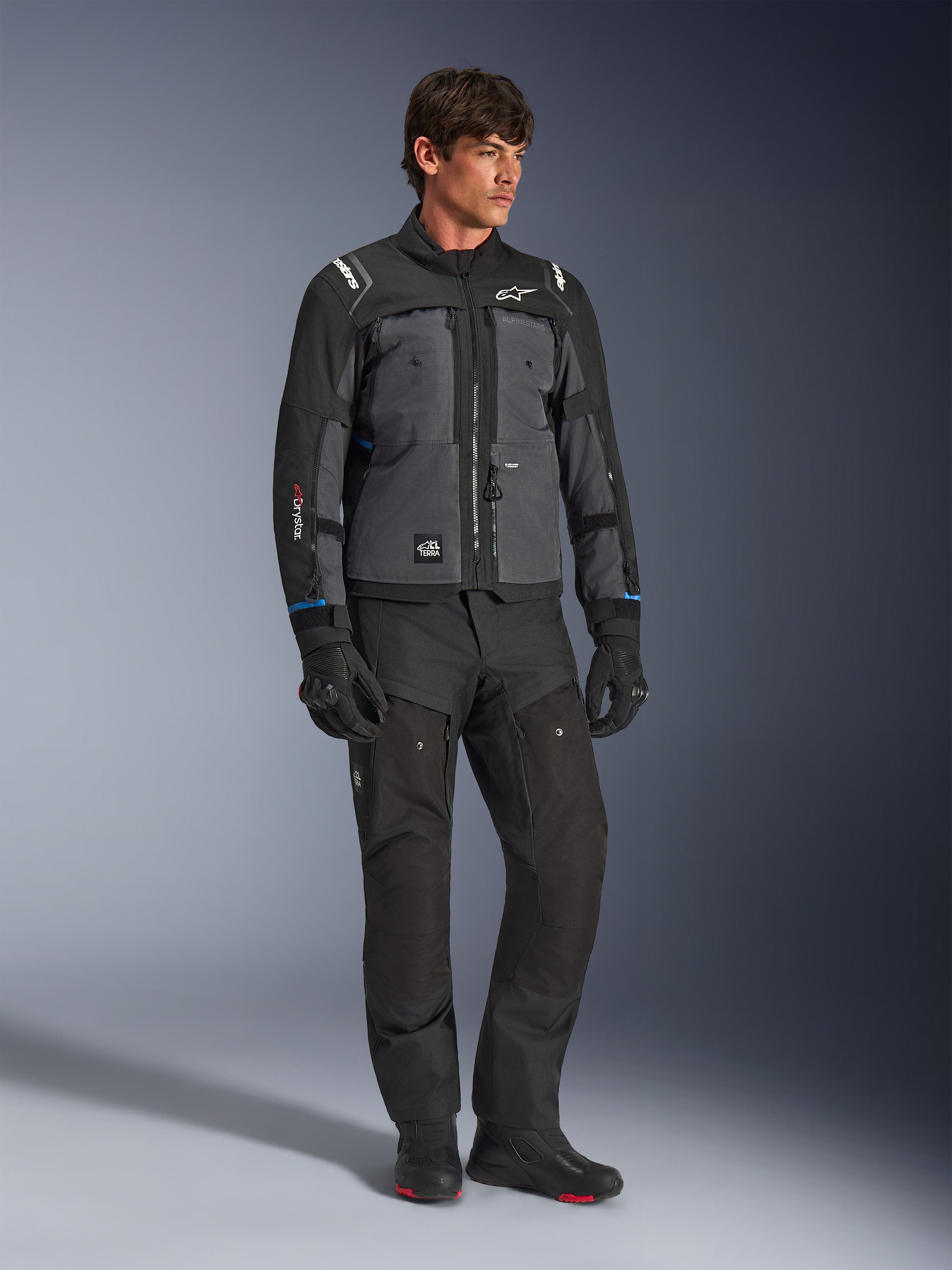 Chaqueta Alpinestars Cusco Drystar® en color negro y gris oscuro, chaqueta técnica de touring para moto con paneles de varios tonos, combinada con pantalones y guantes negros a juego, diseñada para conducción en carretera y adventure touring.