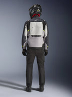Motociclista visto desde atrás vistiendo la chaqueta Alpinestars Cusco Drystar® en Ice Gray, Mid Gray y Deep Gray, con un gran panel de ventilación trasero y marca Alpinestars, combinada con pantalones de moto negros y un casco negro, ropa de motociclismo para adventure touring.