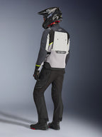 Chaqueta Alpinestars Cusco Drystar® en gris hielo, gris medio y gris oscuro, vista posterior en un motociclista. Presenta detalles en amarillo fluorescente, un amplio panel de ventilación trasero con la marca y tejido resistente. Se complementa con pantalones de moto negros y un casco de aventura para un look de touring completo.