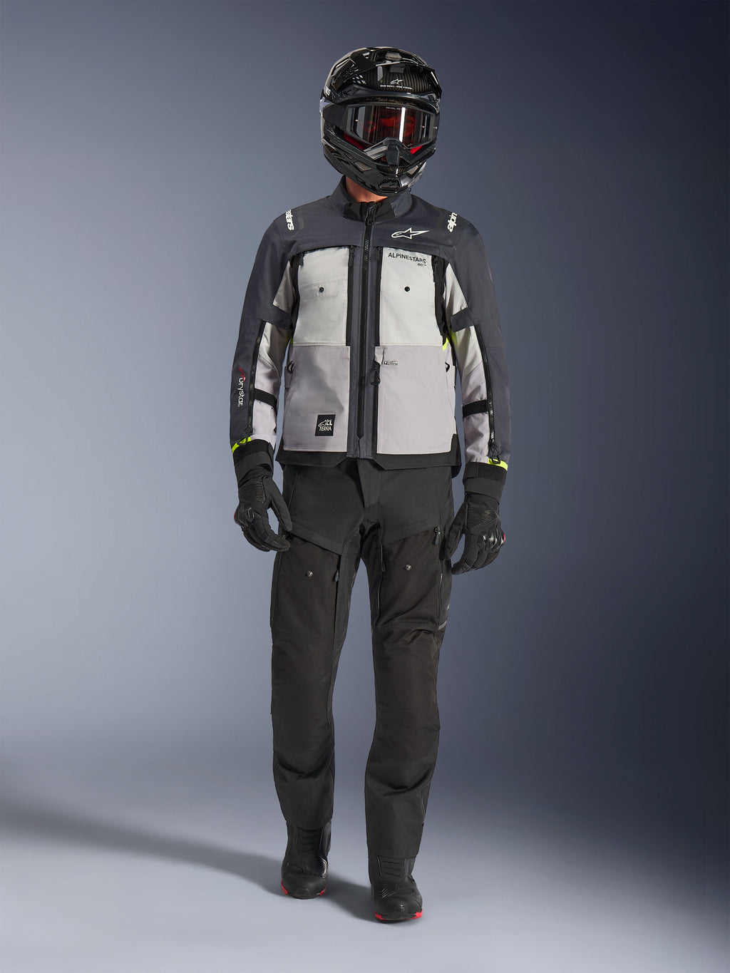 Chaqueta Alpinestars Cusco Drystar®, Ice Gray Mid Gray Deep Gray, chaqueta de motociclismo adventure combinada con pantalones de moto negros, guantes negros y casco negro con gafas, con paneles grises en bloques de color y detalles técnicos para touring y carretera