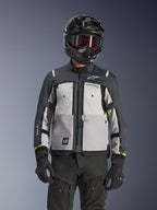 Alpinestars Cusco Drystar® Jacket, chaqueta de adventure touring, en colores Ice Gray, Mid Gray y Deep Gray, con paneles grises de varios tonos, ventilaciones de pecho con cremallera y marca Alpinestars, lucida por un motociclista con casco negro y gafas.
