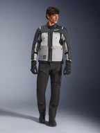 Chaqueta Alpinestars Cusco Drystar® en colores Ice Gray, Mid Gray y Deep Gray, combinada con pantalones y guantes negros de motociclismo de aventura, chaqueta textil de touring con paneles grises multitono y acentos en amarillo neón, fotografía de estudio de modelo masculino.