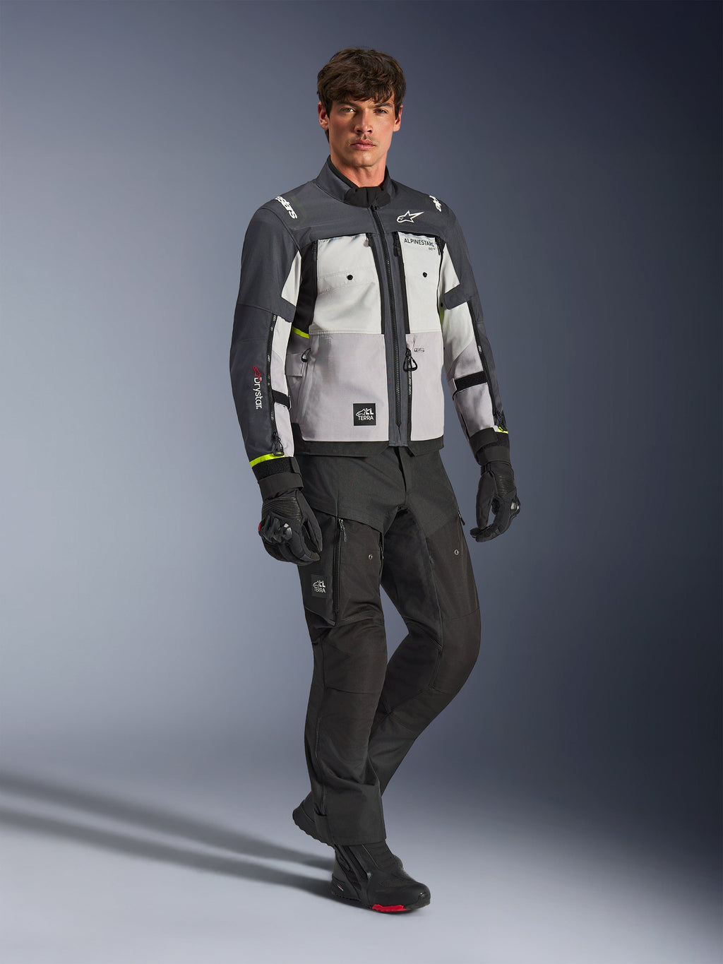 Chaqueta Alpinestars Cusco Drystar®, chaqueta de aventura para motocicleta, colores Ice Gray, Mid Gray y Deep Gray, usada por un modelo con pantalones y guantes negros, paneles grises multitono con construcción textil resistente, ventilaciones con cremallera y logotipos de Alpinestars, fotografía de estudio profesional de equipo para carretera y aventura