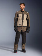 Chaqueta Alpinestars Cusco Drystar® en color Walnut Aluminum Black, vestida por un piloto masculino con pantalones de aventura touring a juego, guantes negros y botas, con paneles beige en el pecho, mangas negras con sutiles detalles en naranja y cremalleras de ventilación funcionales para la conducción en carretera.