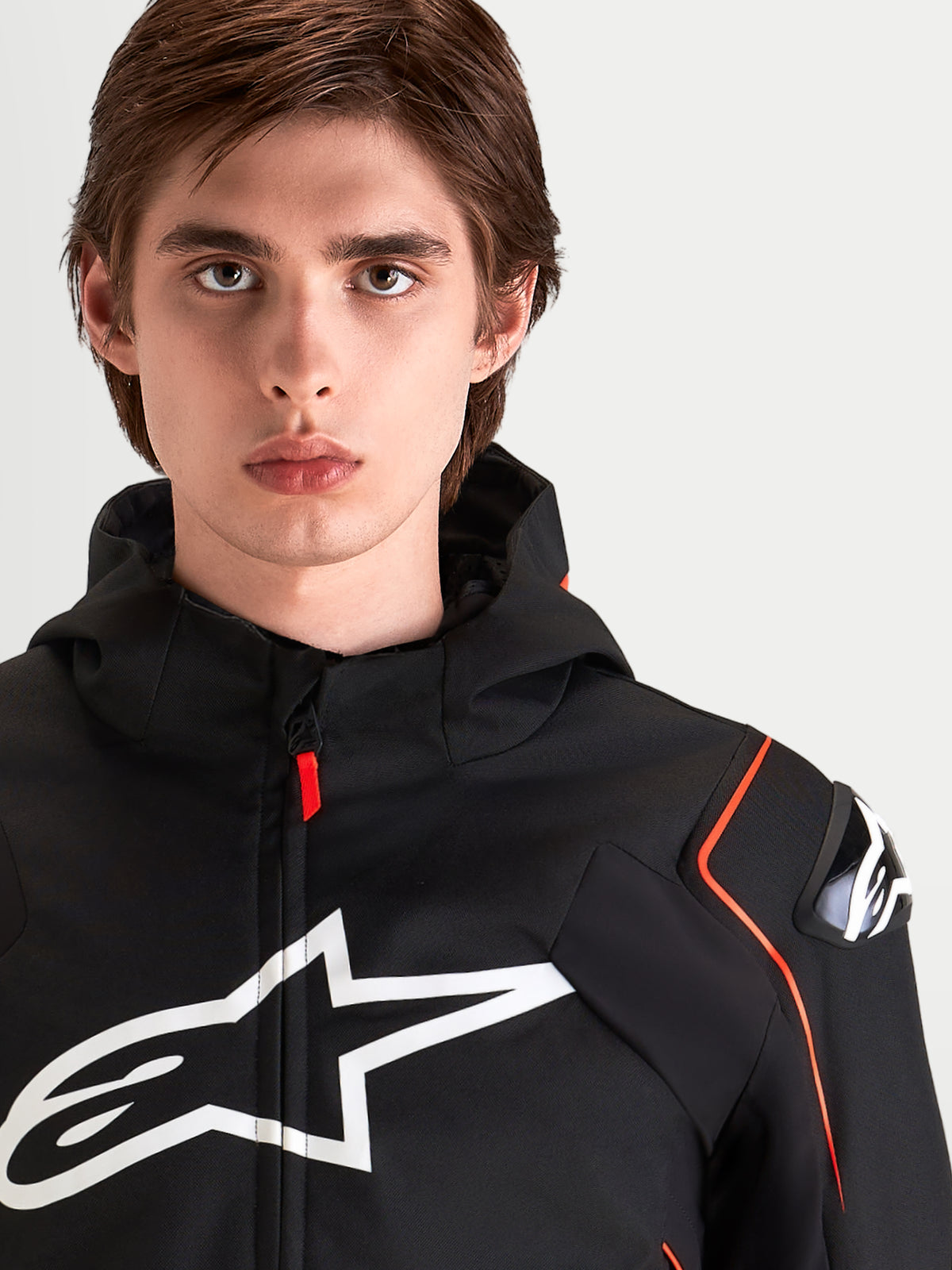 Alpinestars Zaca V 2 Waterproof Jacket, chaqueta de moto deportiva impermeable para hombre, negro y rojo flúor, con protección DFS en los hombros y gran logotipo en el pecho, retrato de cerca de un piloto