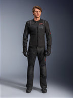 Male model wearing Alpinestars ST-2 Air Jacket, Black motorcycle jacket with mesh panels and red logo, 'Alpinestars Exploration Equipment' text on chest, paired with black technical riding pants and gloves, modern adventure touring gear
