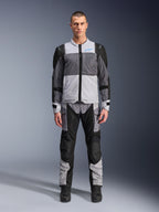 Chaqueta Alpinestars ST-2 Air, chaqueta de touring para moto, en gris hielo, gris oscuro y negro, vestida por un modelo con pantalones de aventura a juego, con grandes paneles de malla, logotipo de Alpinestars azul en el pecho y marca Alpinestars Exploration Equipment.