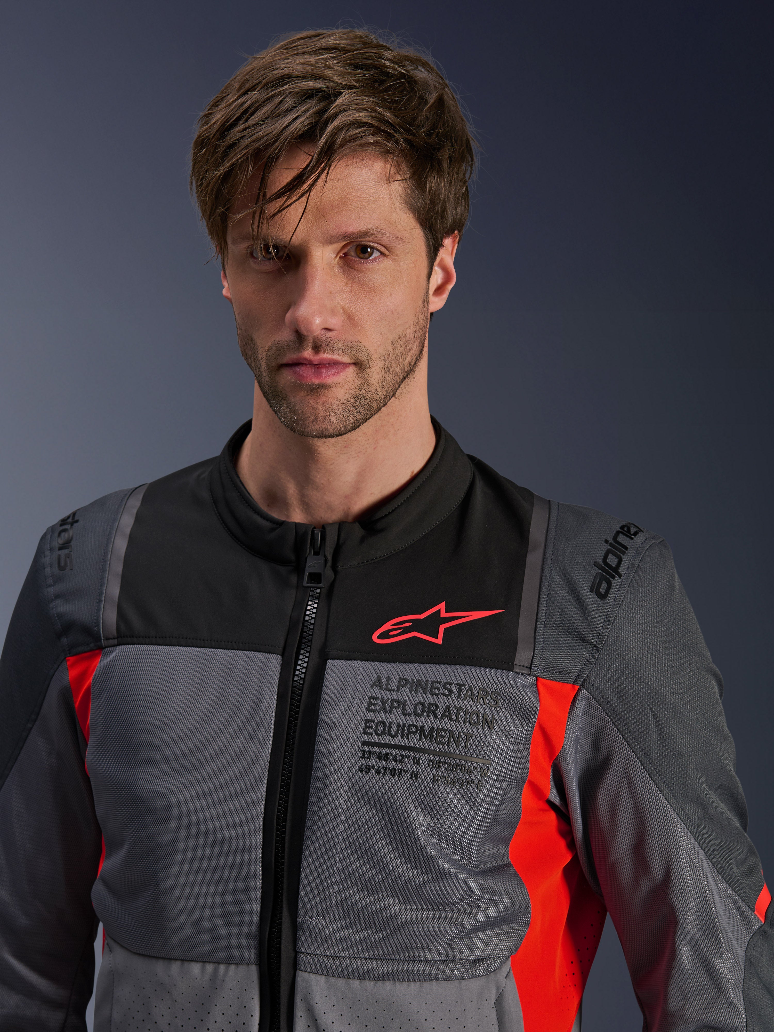 Alpinestars ST-2 Air Jacket, Deep Gray Dark Gray and Bright Red, summer touring motorcycle jacket worn by a model, featuring mesh ventilation panels, red Astars logo, and 'Exploration Equipment' branding on the chest.