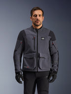 Alpinestars Maxdura Drystar®XF Laminated Armored Shell, chaqueta de moto de aventura en gris oscuro y negro, vista frontal en modelo, con grandes bolsillos de carga, logotipo 'All Terra' en el pecho y cremalleras de ventilación, combinada con guantes y pantalones de montar negros.